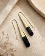 Tosha brass horn threader earrings flat-lay on stone surface, gold fluted cone with black horn drop detail