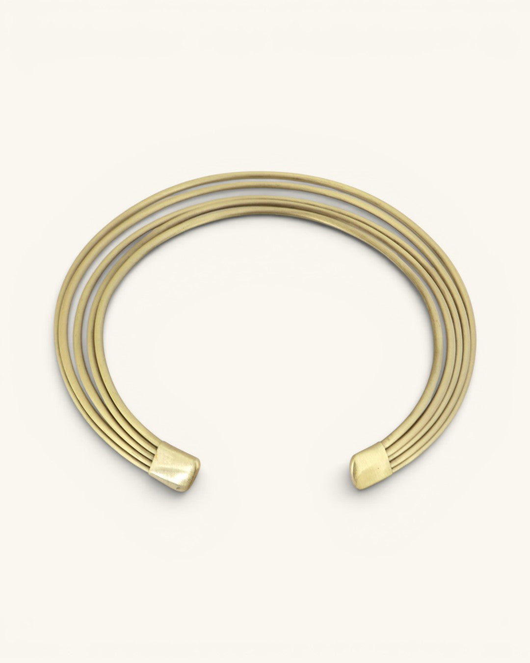 Brass multi-band collar necklace on cream background, open-end view with hammered brass end caps visible at both terminals