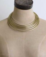 Hand-beaten brass collar necklace on tan fabric dress form, front view showing all five bands spanning the collar and chest