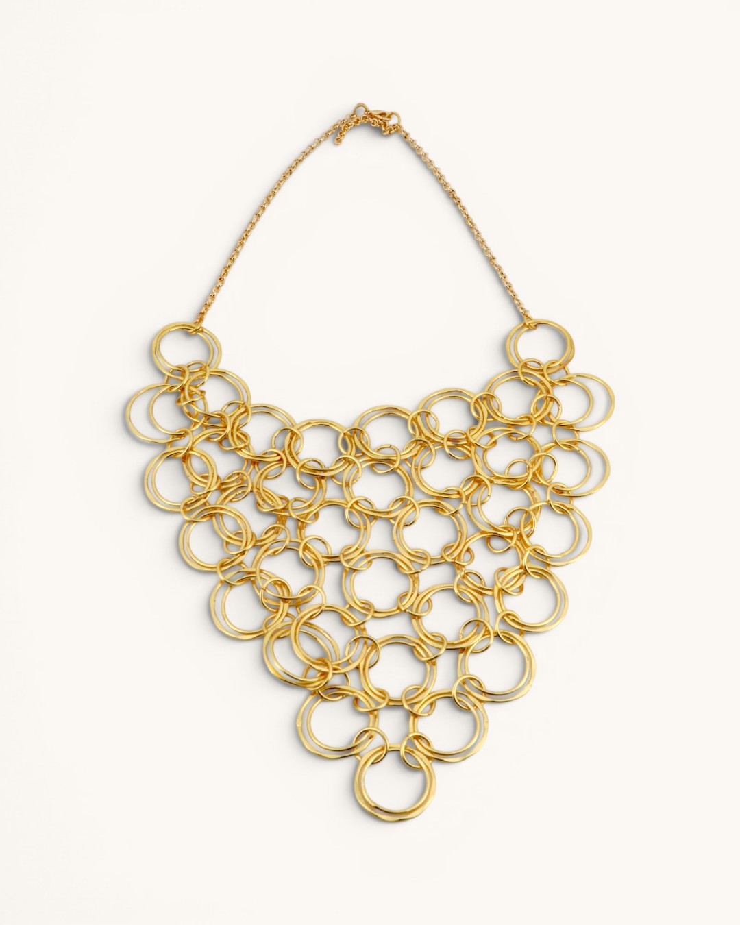 Hand-hammered brass ring bib necklace flat lay on white background showing full chain with clasp and triangular bib