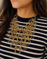 Brass ring bib necklace worn by a model over a navy and white striped sweater, showing full drape on the chest