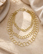 Brass three-strand circular link chain necklace flat lay on stone surface with toggle clasp visible, warm styled shot