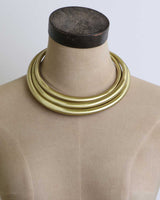 Hand-beaten brass triple-strand collar necklace on a tan dress form mannequin, angled front view showing fit