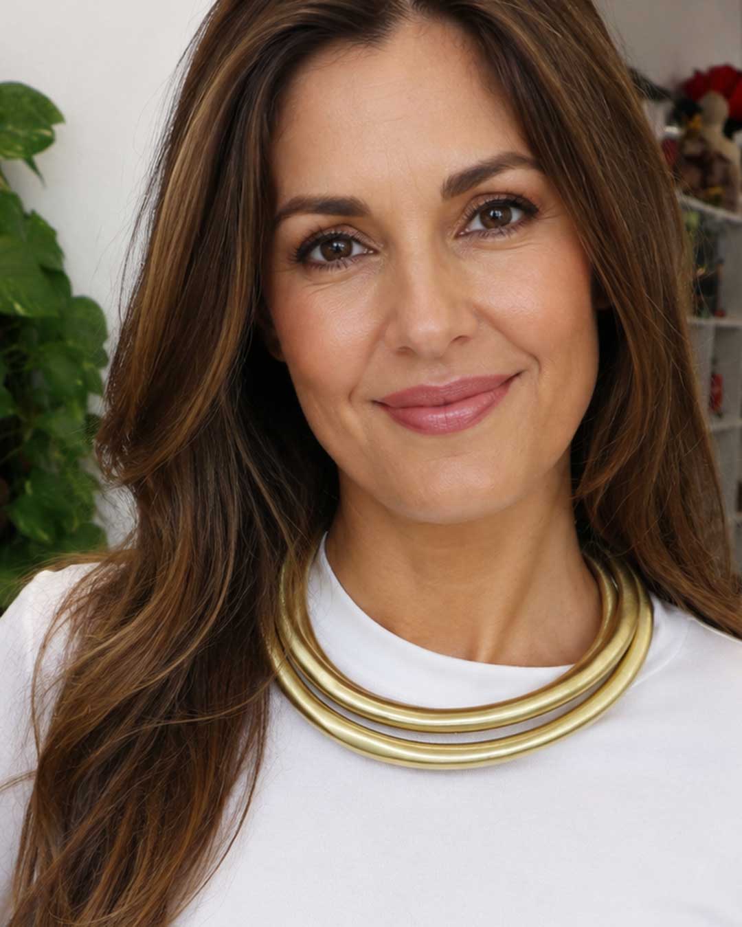 Hand-beaten brass triple-strand collar necklace worn by a woman over a white top, close-up front view