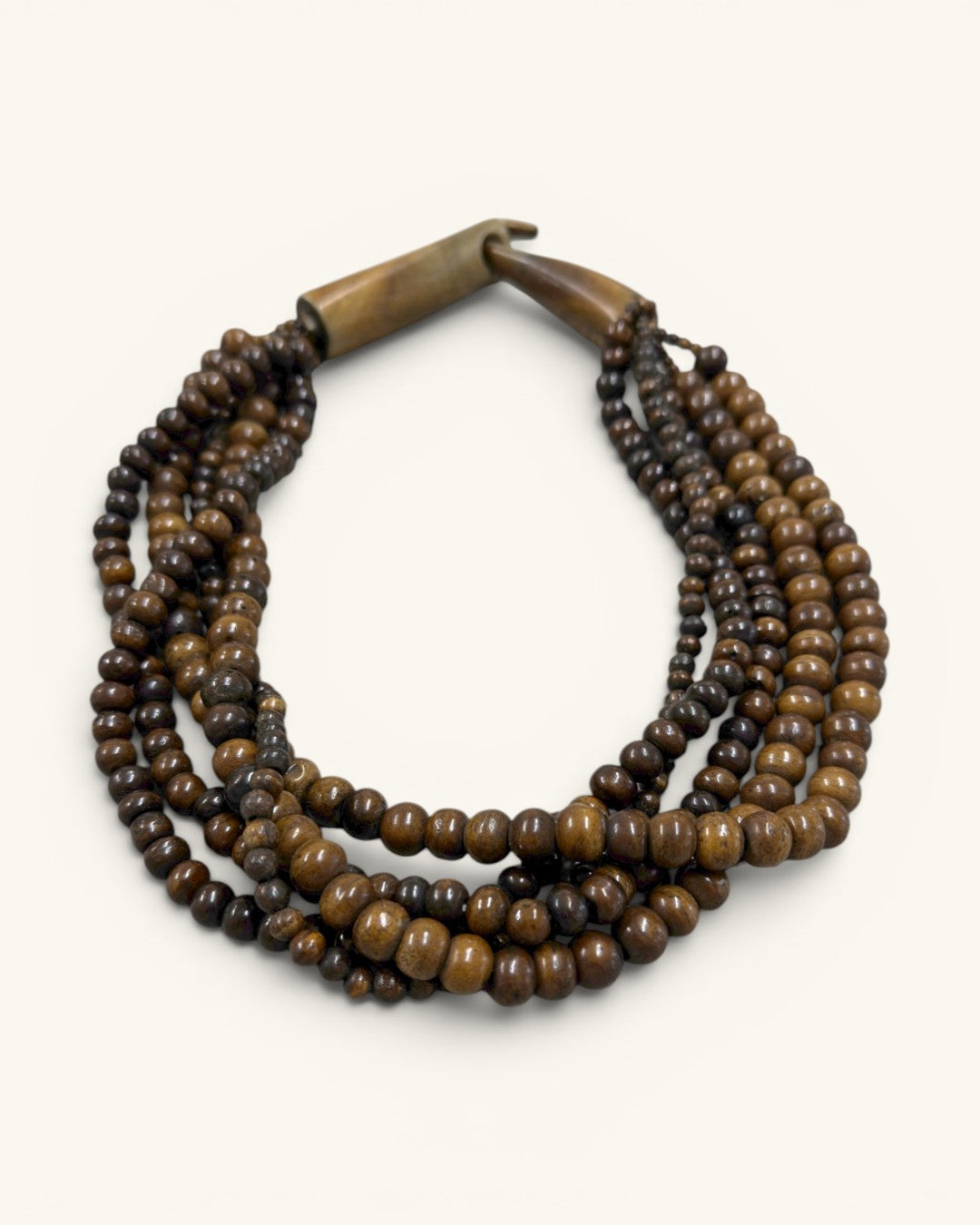 Brown five-strand beaded necklace in angled flat lay on cream background, wooden clasp positioned upper left