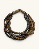 Brown five-strand beaded necklace in angled flat lay on cream background, wooden clasp positioned upper left