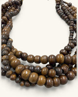 Close-up detail of varied-size brown wooden beads across five strands, showing surface texture and mixed sizing