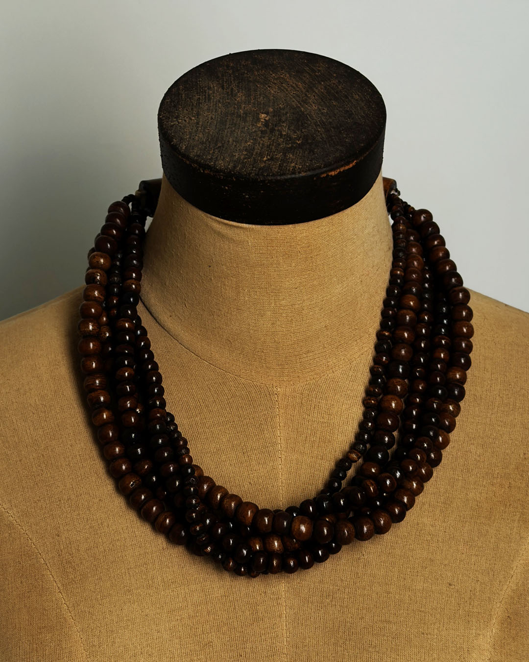 Brown five-strand beaded necklace displayed on a burlap dress form mannequin, front view showing drape and fall