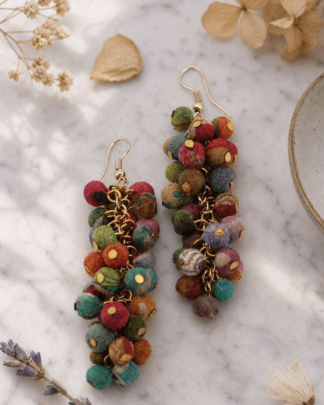 Handmade kantha cluster earrings with colorful recycled textile patches displayed on white marble surface