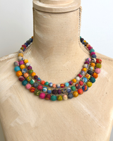Colorful textile-wrapped bead layered necklace displayed on a tan fabric dress form, showing three-row bib drape