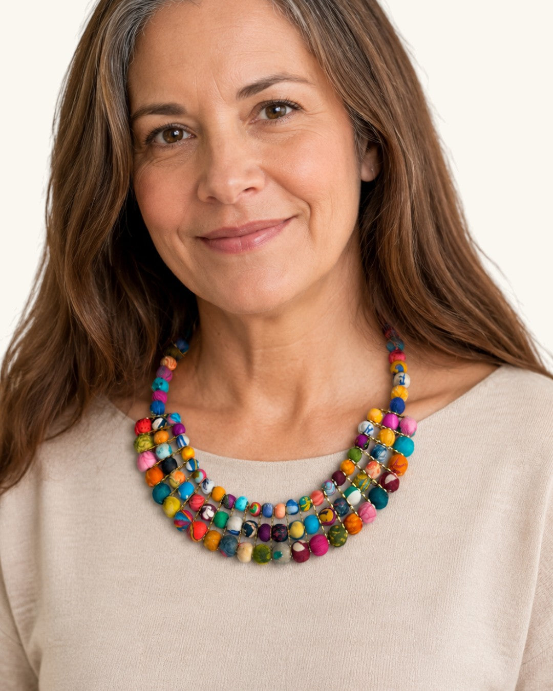 Colorful textile-wrapped bead layered necklace worn by smiling brown-haired woman in cream top, showing neckline drape