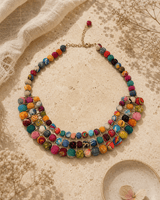 Layered necklace with colorful textile-wrapped beads displayed on travertine surface