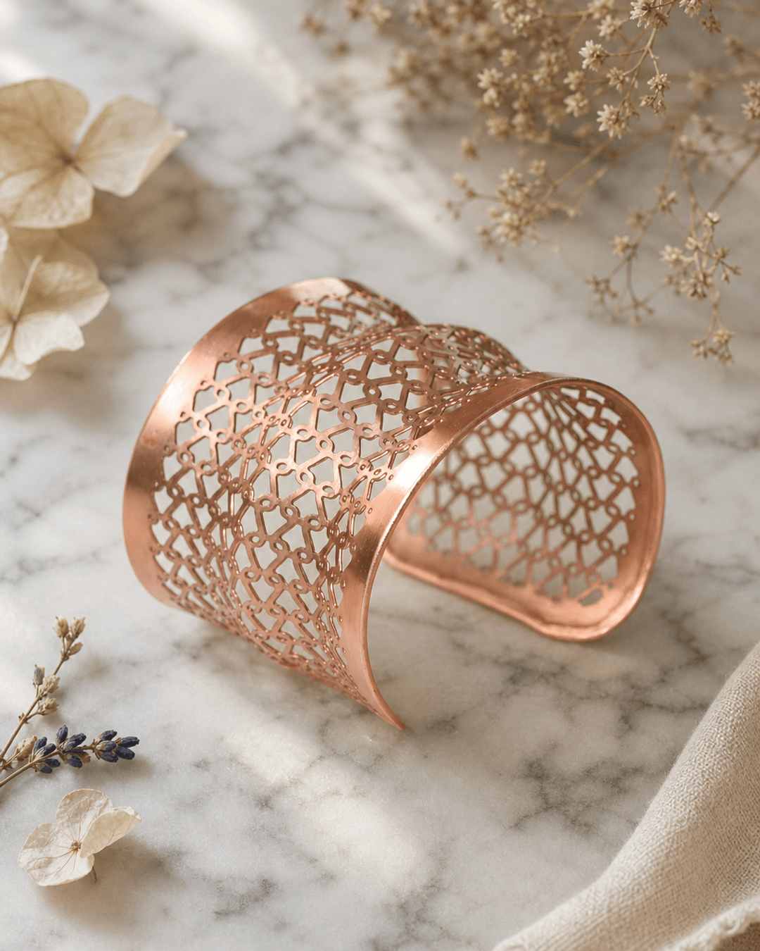 Copper wide cuff bracelet with geometric lattice pattern displayed on white marble surface