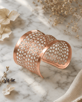 Copper wide cuff bracelet with geometric lattice pattern displayed on white marble surface