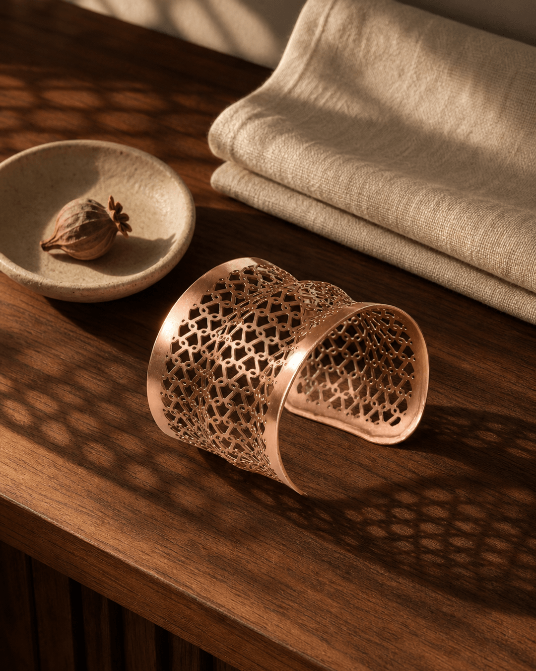 Copper wide cuff bracelet with geometric lattice pattern displayed on a wooden console surface