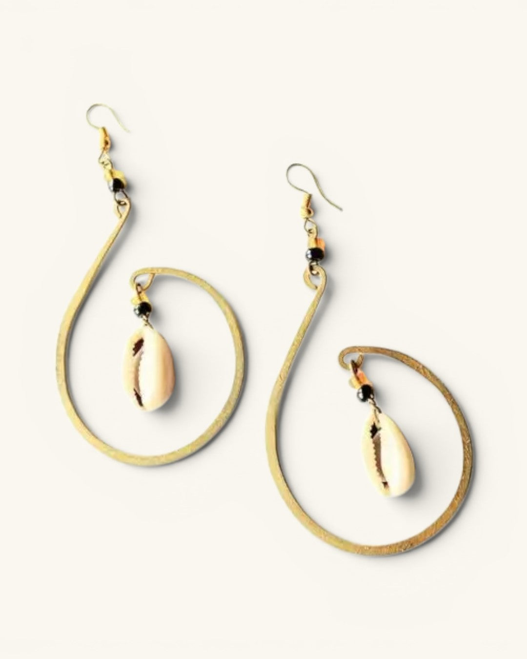 Mombasa hammered brass hoop earring pair on white background, spread apart to show hammered texture and dangling cowrie shells