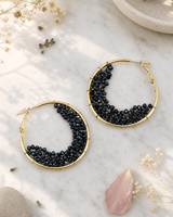 Black beaded crescent hoop earrings displayed on white marble surface