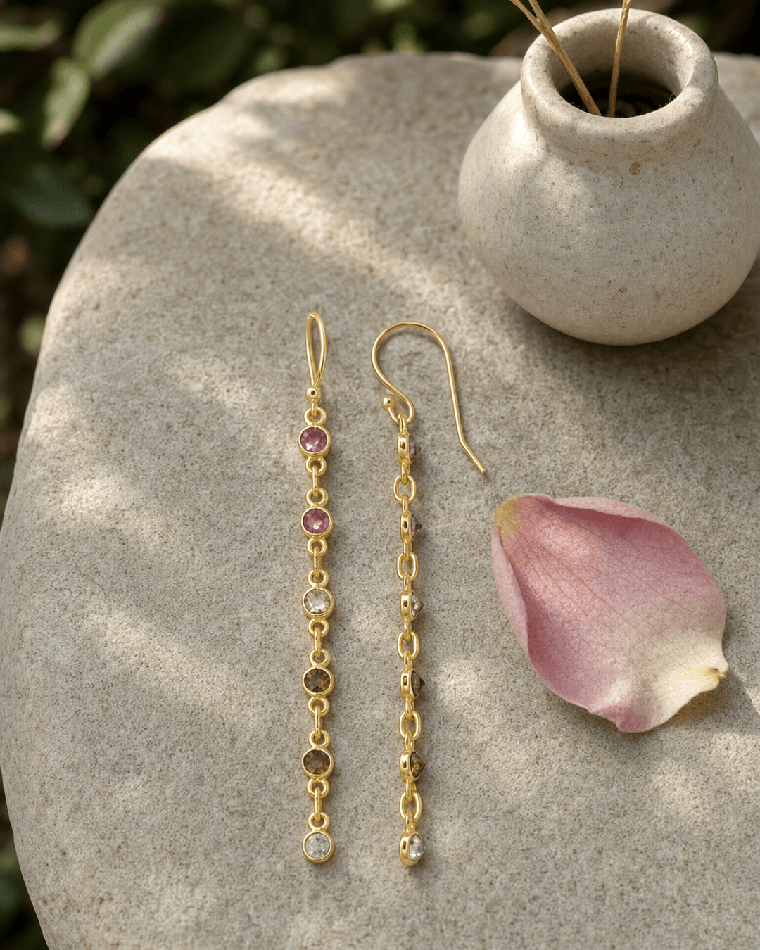 Dainty multi-color tourmaline dangle earrings displayed on a textured garden stone surface