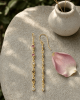 Dainty multi-color tourmaline dangle earrings displayed on a textured garden stone surface