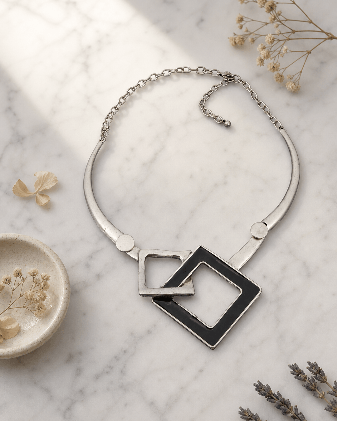 Gold geometric statement necklace with angular pendant on white marble surface