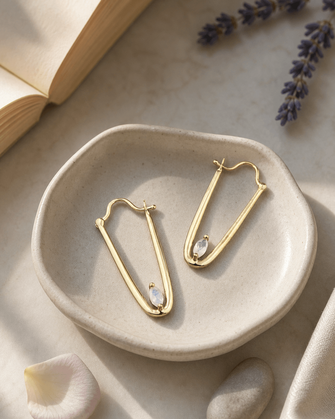 Gold plated moonstone drop earrings displayed on a vanity, showing iridescent blue-white gemstones with delicate gold hardware