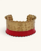 Hand-hammered brass cuff bracelet with red painted lower band and scalloped edges, straight-on front view on white background