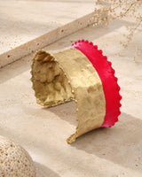 Hand-hammered brass cuff bracelet with red painted band displayed upright on stone surface with dried botanicals in background