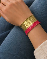 Hand-hammered brass cuff bracelet with red painted band worn on a model's wrist against denim jeans, side view