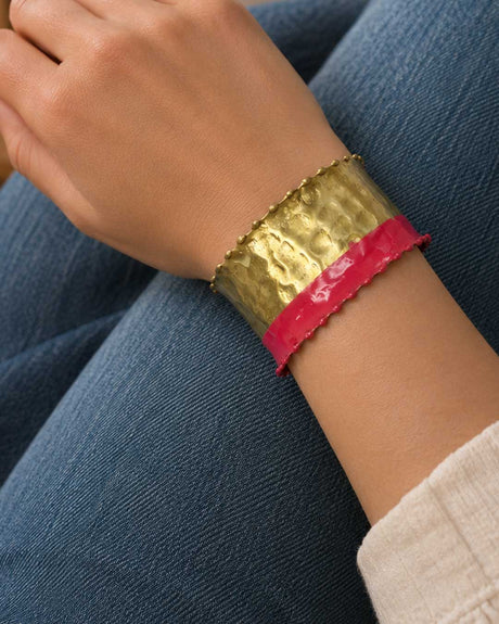 Hand-hammered brass cuff bracelet with red painted band worn on a model's wrist against denim jeans, side view