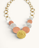 Hammered tri-tone disc necklace detail showing graduated brass, copper, and silver discs with gold ring chain on white background