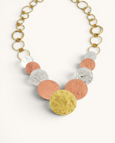 Hammered tri-tone disc necklace detail showing graduated brass, copper, and silver discs with gold ring chain on white background