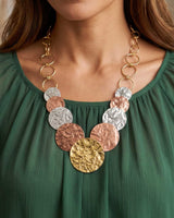 Hammered Brass & Copper Tri-Tone Disc Necklace worn by a model in a green ruffled top, showing drape and scale across the neckline
