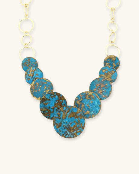 Hand-forged brass statement necklace with blue patina discs, angled view highlighting individual disc pendants and brass links