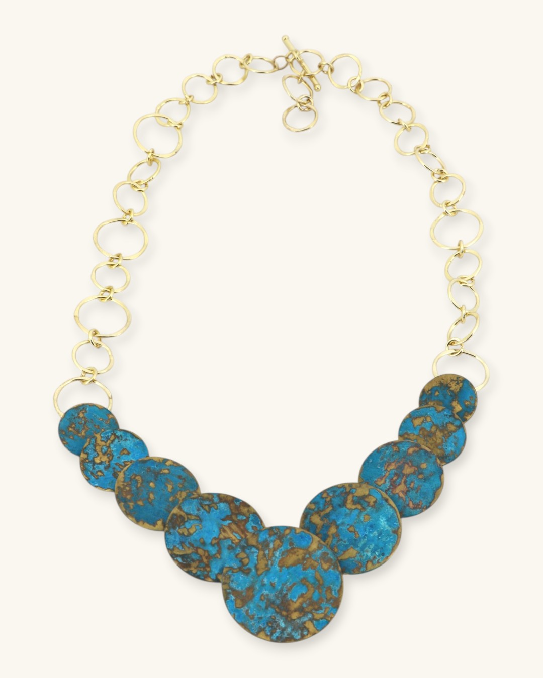 Hand-forged brass statement necklace with blue patina discs, angled front view showing chain texture and forged brass detailing
