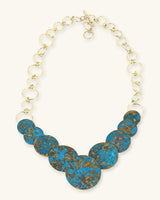 Hand-forged brass statement necklace with blue patina discs, angled front view showing chain texture and forged brass detailing