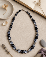 Hand-Painted Black Ceramic Pottery Bead Necklace with Metal Accents — necklaces, flatlay linen lifestyle photo