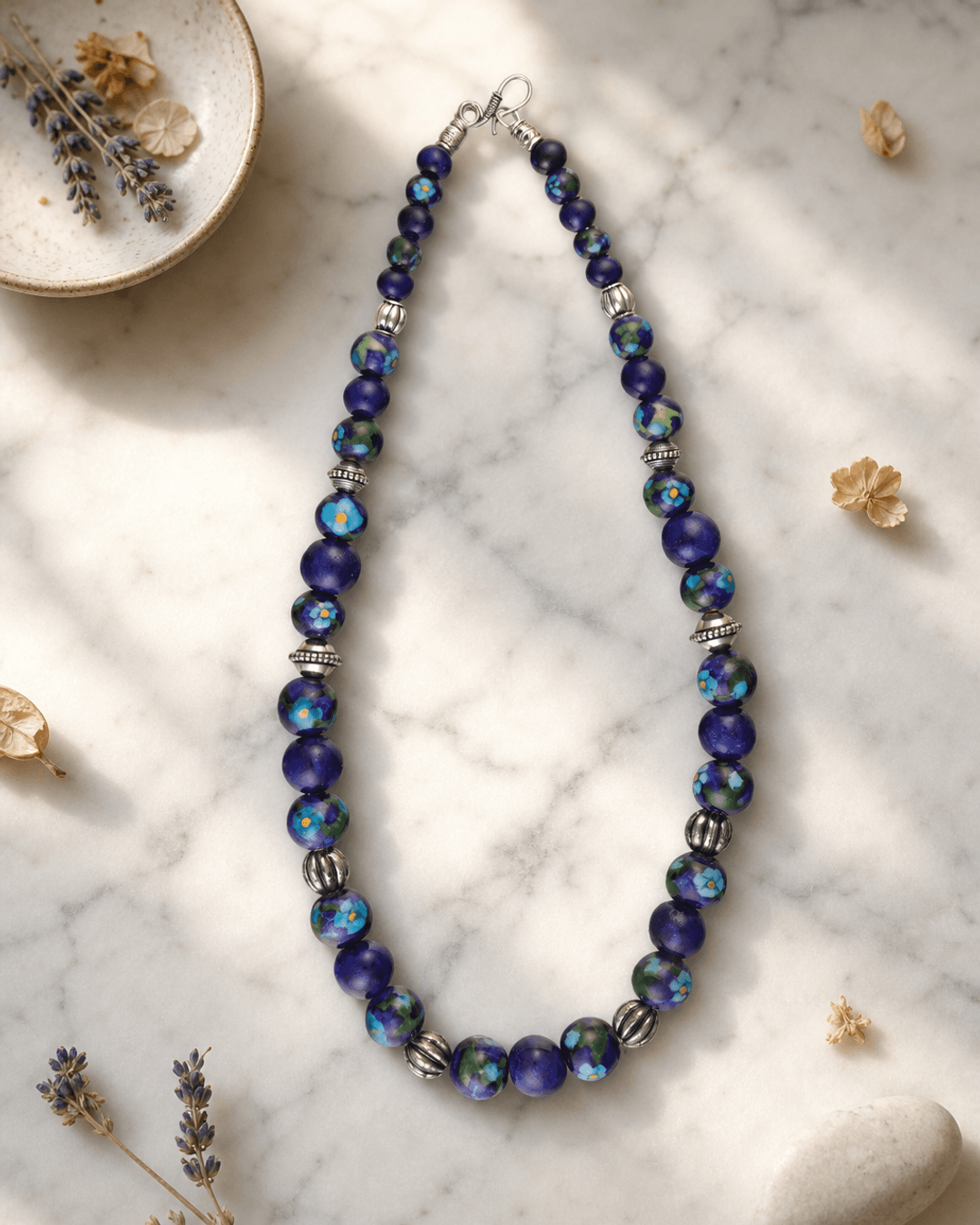 Hand-Painted Blue Pottery Bead Necklace with Floral Patterns — necklaces, editorial marble lifestyle photo