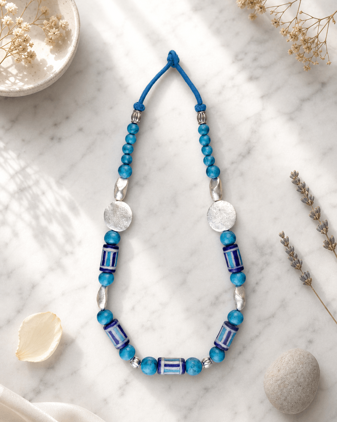 Hand-Painted Blue Pottery Bead Necklace with Metal Accents — necklaces, editorial marble lifestyle photo