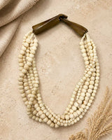 Indian bone bead 5-strand layered necklace with horn closure flat lay on sandy stone surface with linen and dried grass