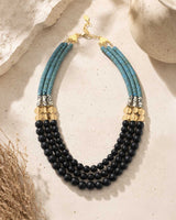 Jet glass and hematite triple strand necklace laid flat on stone surface with dried grass props, full layout and gold clasp visible