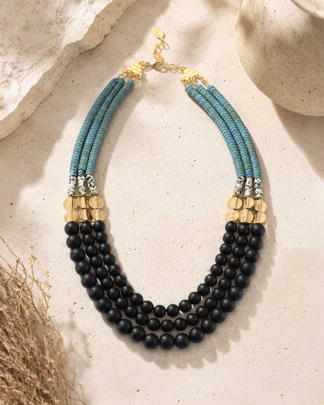 Jet glass and hematite triple strand necklace laid flat on stone surface with dried grass props, full layout and gold clasp visible