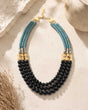 Jet glass and hematite triple strand necklace laid flat on stone surface with dried grass props, full layout and gold clasp visible