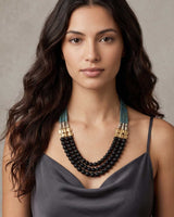 Jet glass and hematite triple strand necklace worn by a model in a gray satin top, three black bead strands falling at chest