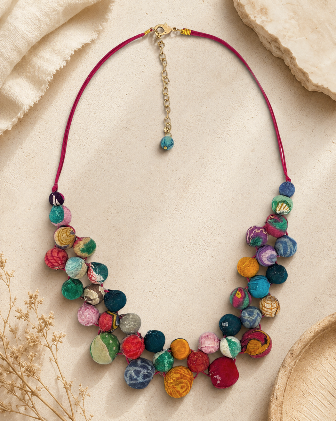 Kantha recycled bead necklace on sandy surface with dried grasses, showing two layers of multicolor kantha fabric beads and gold extender chain