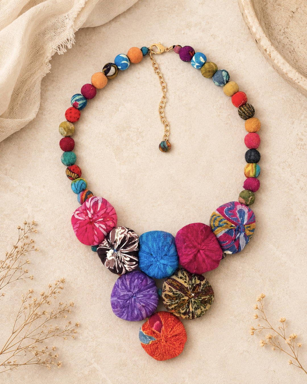 Kantha recycled textile layered bead necklace styled on a sandy surface with dried botanicals, showing full length with gold extender chain