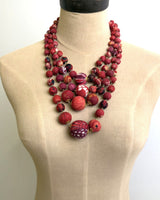 Four-strand red kantha sari bead necklace draped on a tan linen dress form showing full length and layered drop