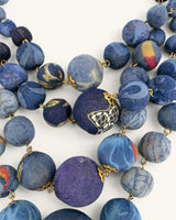 Close-up detail of blue kantha sari fabric beads with printed and marbled patterns, connected by gold wire and findings