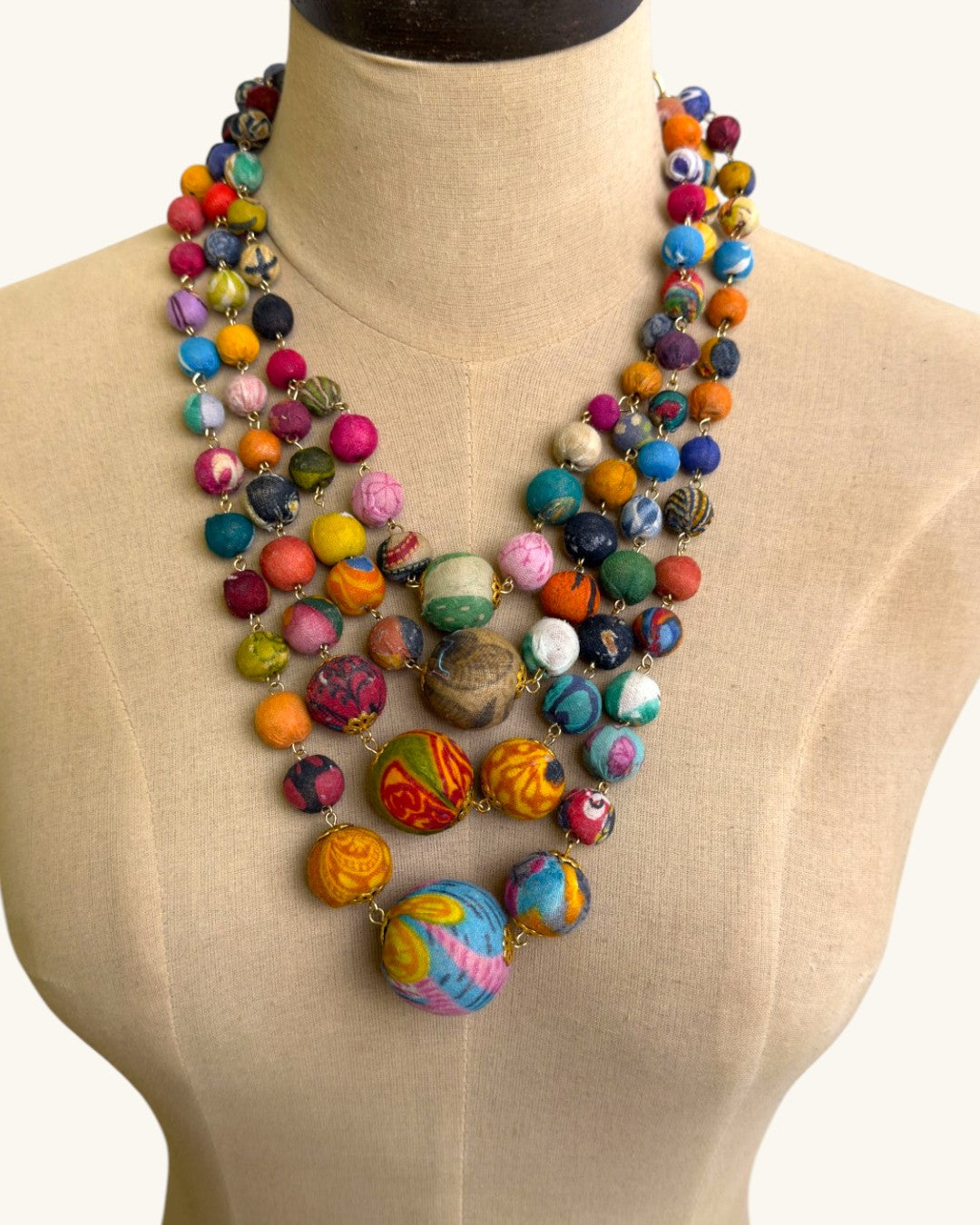 Kantha recycled textile four-strand statement necklace on a beige dress form showing graduated bead sizing and full drape