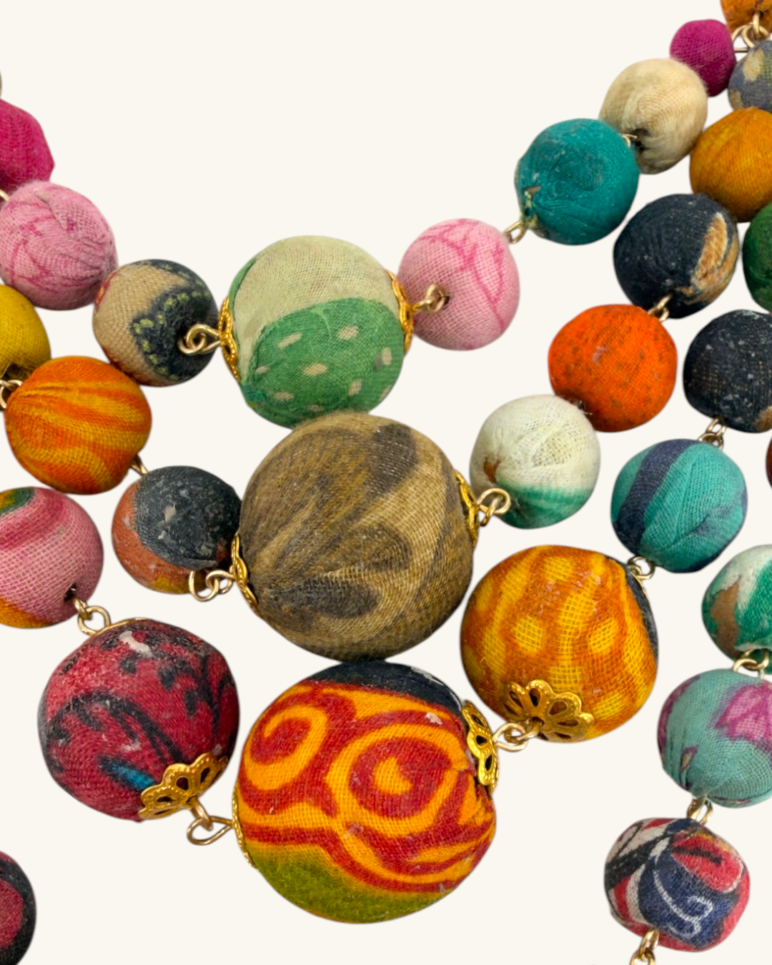 Close-up detail of kantha recycled textile necklace showing varied fabric patterns and gold connector links between beads