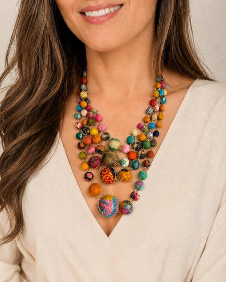 Kantha four-strand statement necklace worn by a model in a cream v-neck top, showing layered multicolor fabric beads